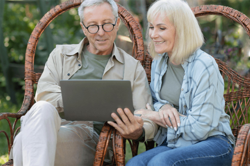 Senior couple sit outside reading about assisted living on laptop