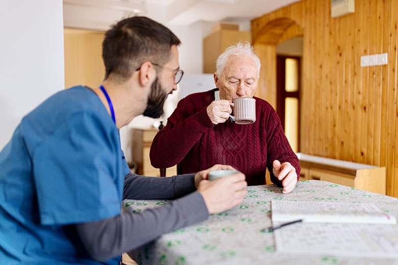 Male nurse drinks coffee with elderly man